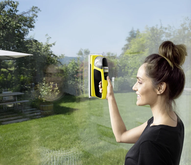 Žena čistí okno žlutým elektrickým mytím oken venku.