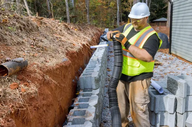 Stavebník staví opěrnou zeď z betonových bloků.